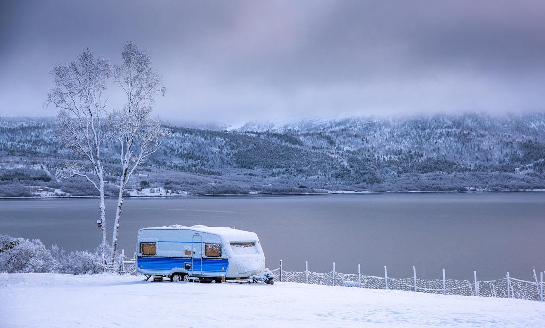 Travel trailer parked in the snow by a lake