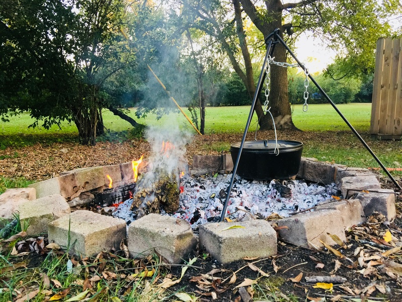 People cook outside with a Dutch oven suspended over a campfire. 