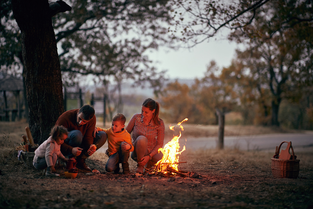 A family ready to cook outside around a campfire in the forest.