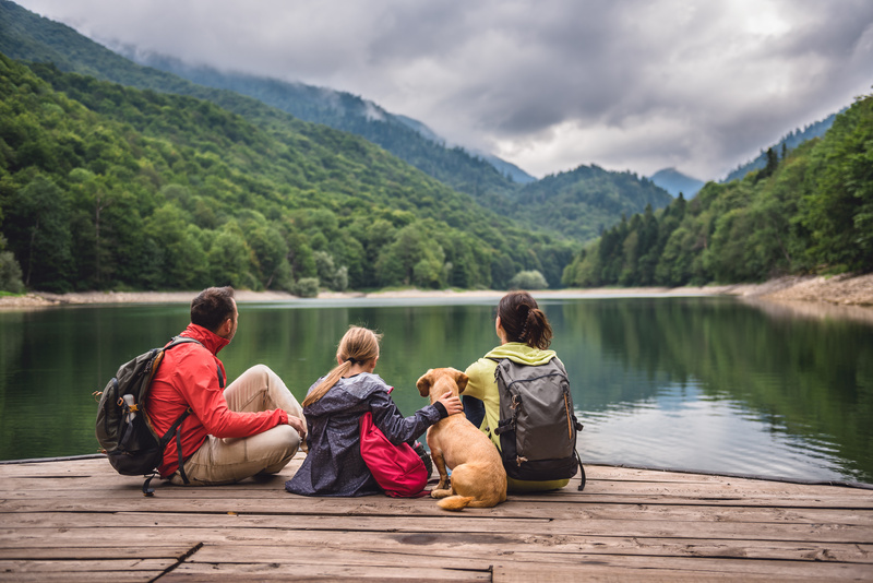 Family with a small yellow dog resting on a pier and looking at lake and foggy mountains.